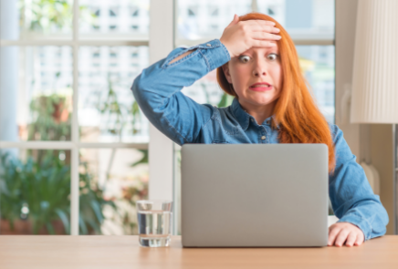Woman sitting in front of laptop with a hand on her forehead and stressed expression on her face.